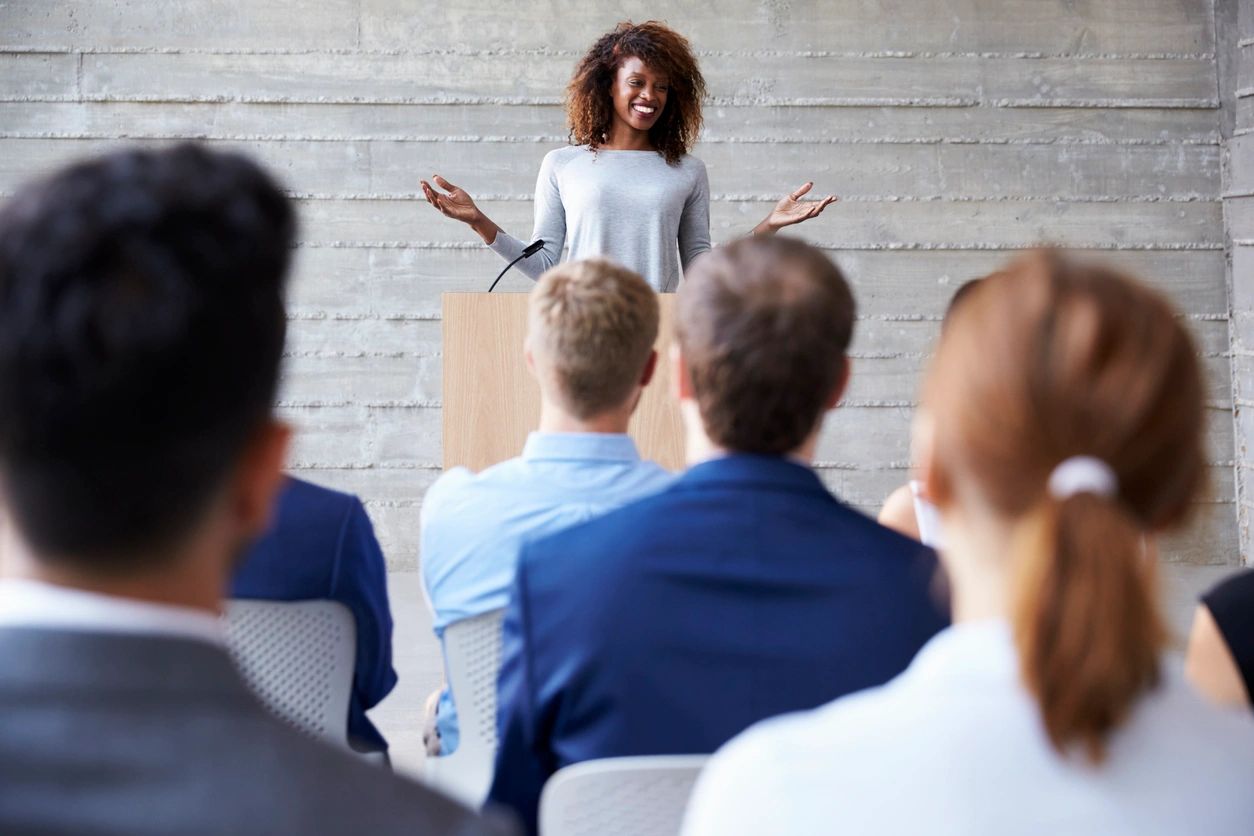 Woman speaking passionately at a podium to a small audience.